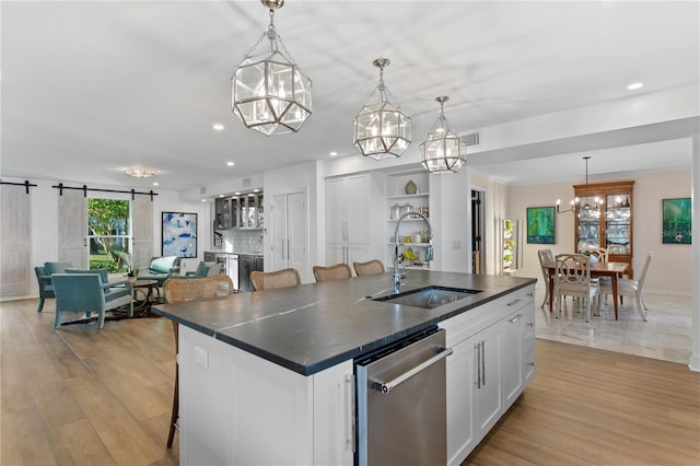 kitchen with sink, white cabinetry, decorative light fixtures, stainless steel dishwasher, and an island with sink