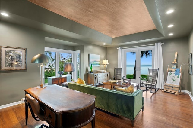 interior space featuring hardwood / wood-style floors, a raised ceiling, french doors, and a water view