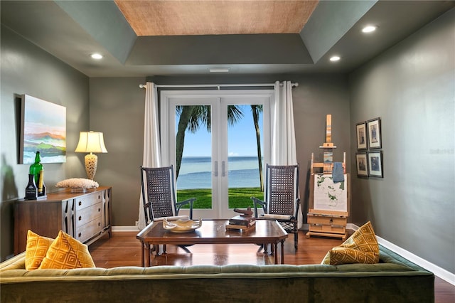 living area with dark hardwood / wood-style flooring, a tray ceiling, french doors, and a water view