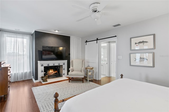 bedroom with dark wood-type flooring, ceiling fan, and a barn door