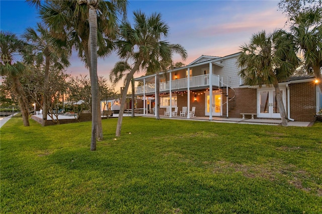 back house at dusk featuring french doors, a balcony, a yard, and a patio