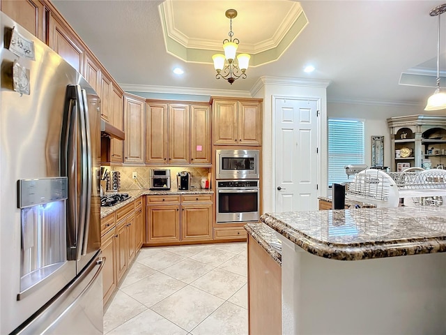 kitchen with appliances with stainless steel finishes, pendant lighting, a raised ceiling, crown molding, and light stone countertops