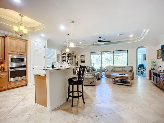 kitchen featuring a raised ceiling, an island with sink, pendant lighting, stainless steel appliances, and light stone countertops