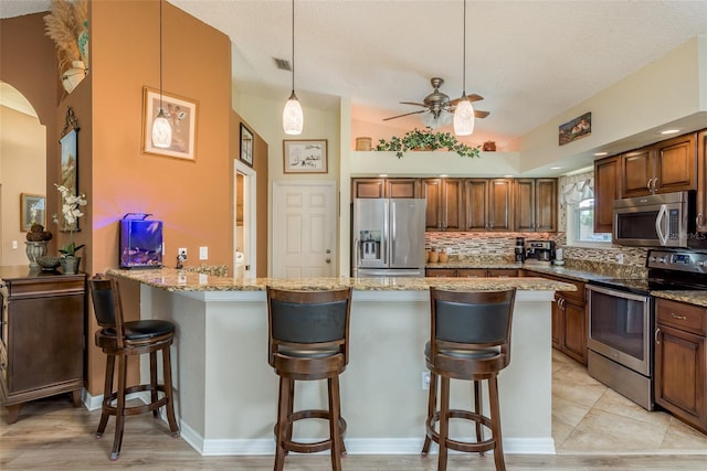 kitchen featuring stainless steel appliances, light stone countertops, pendant lighting, and a kitchen breakfast bar