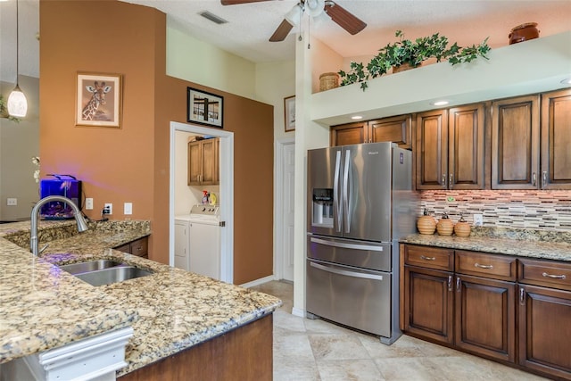 kitchen with sink, light stone counters, tasteful backsplash, stainless steel fridge, and washer and clothes dryer