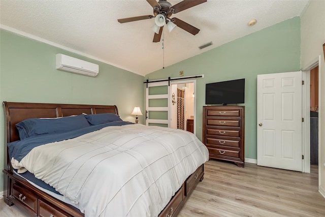 bedroom with lofted ceiling, light hardwood / wood-style flooring, a wall mounted air conditioner, a textured ceiling, and a barn door