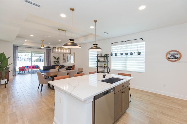 kitchen featuring light stone counters, stainless steel dishwasher, a tray ceiling, and sink