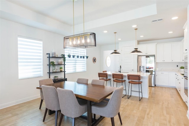 dining space with sink, a wealth of natural light, light hardwood / wood-style flooring, and a raised ceiling