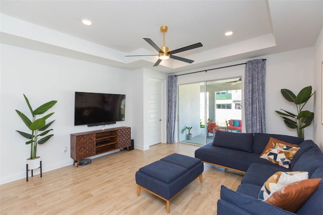 living room featuring ceiling fan, a tray ceiling, and light hardwood / wood-style flooring