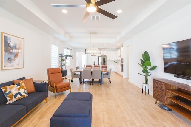 living room featuring a tray ceiling, light hardwood / wood-style flooring, and ceiling fan