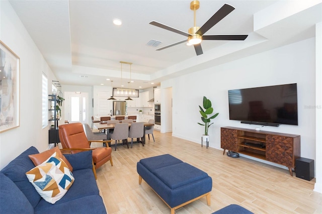 living room featuring a raised ceiling, ceiling fan, and light hardwood / wood-style floors