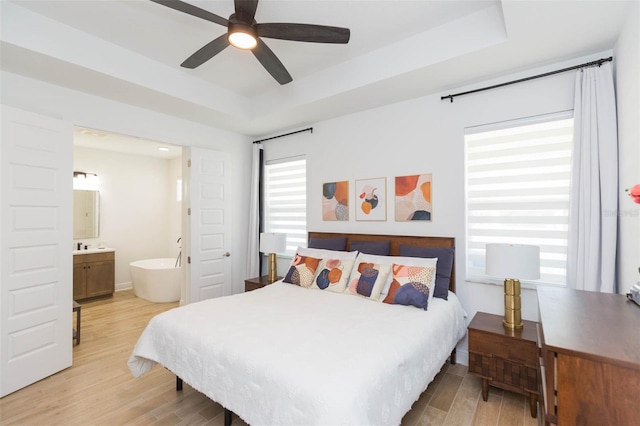 bedroom featuring connected bathroom, a raised ceiling, ceiling fan, and light wood-type flooring