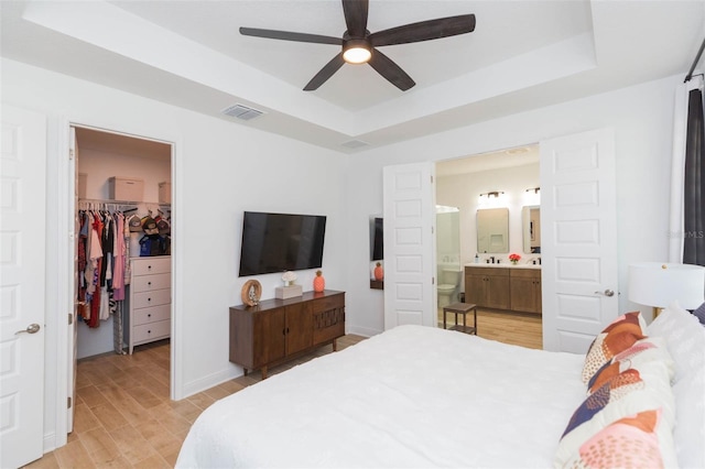 bedroom featuring ensuite bath, light hardwood / wood-style flooring, a tray ceiling, a walk in closet, and a closet