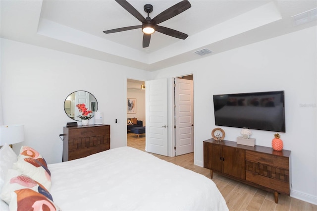 bedroom featuring ceiling fan, light wood-type flooring, and a tray ceiling