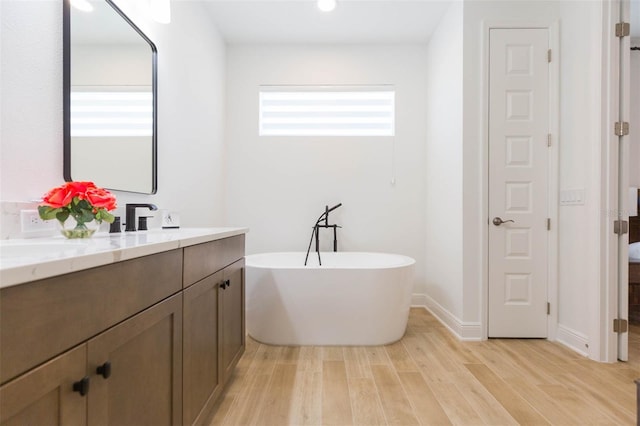 bathroom with a washtub, vanity, and wood-type flooring