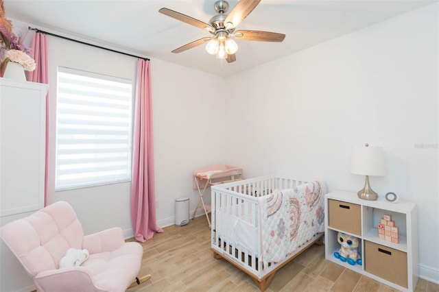 bedroom with a crib, ceiling fan, and light hardwood / wood-style floors