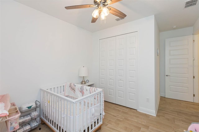 bedroom featuring a nursery area, ceiling fan, a closet, and light wood-type flooring