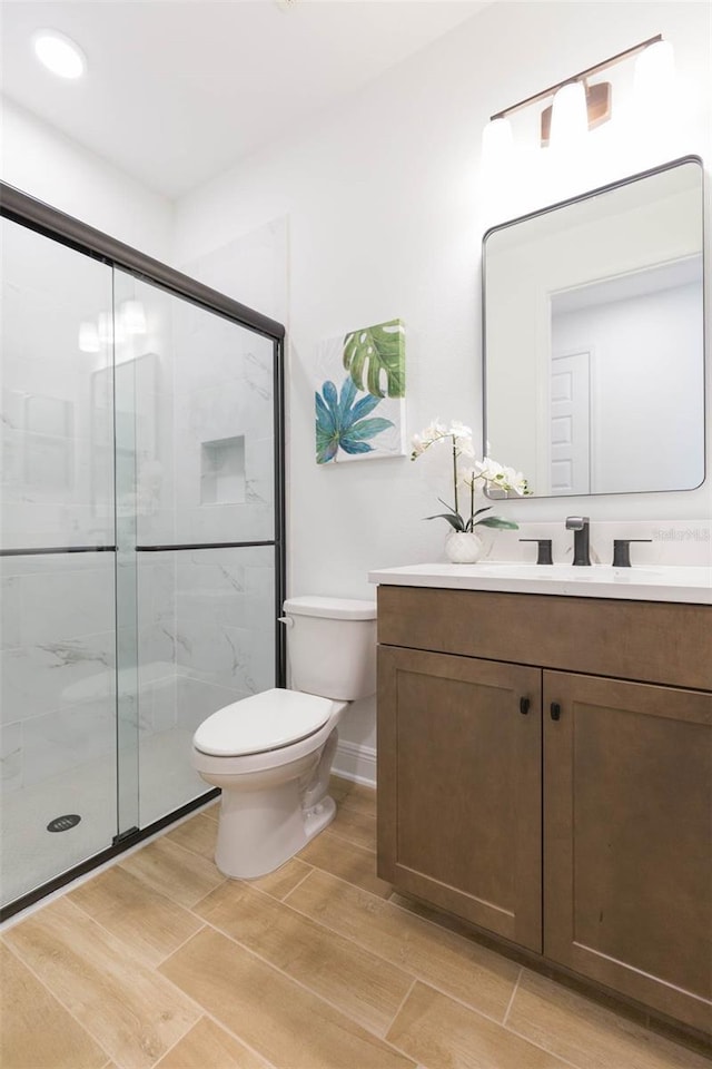 bathroom with a shower with door, vanity, and toilet