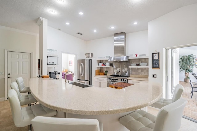 kitchen featuring appliances with stainless steel finishes, sink, backsplash, kitchen peninsula, and wall chimney range hood