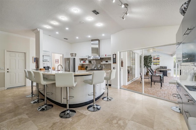 kitchen featuring a breakfast bar, vaulted ceiling, a large island with sink, stainless steel fridge, and wall chimney range hood