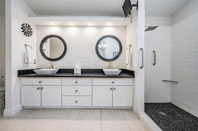 bathroom with tile patterned flooring, tiled shower, vanity, a textured ceiling, and toilet