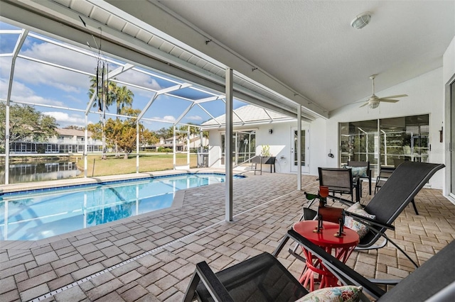 view of pool with a patio, a water view, ceiling fan, and glass enclosure