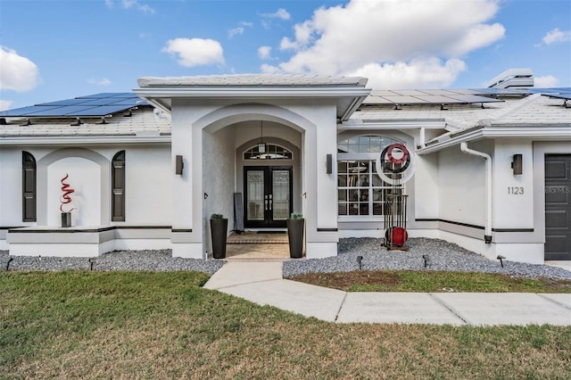 doorway to property with french doors, solar panels, a garage, and a lawn