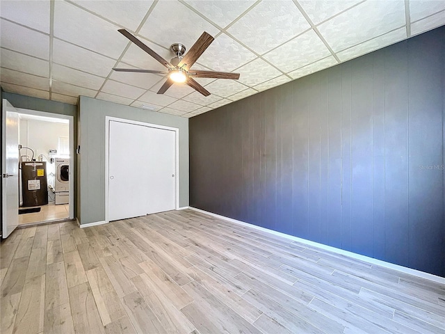 unfurnished bedroom featuring light hardwood / wood-style flooring, ceiling fan, washer / clothes dryer, water heater, and a drop ceiling