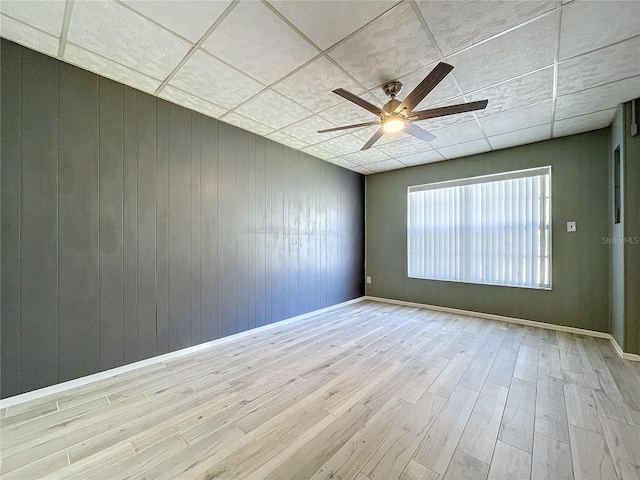 spare room with ceiling fan, wooden walls, light hardwood / wood-style flooring, and a drop ceiling