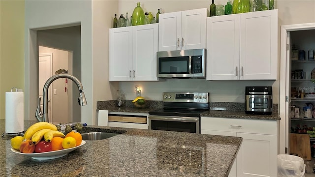 10854 Sage Canyon Dr, Riverview, FL 33578 - kitchen featuring appliances with stainless steel finishes, dark stone counters, white cabinets, and a sink
