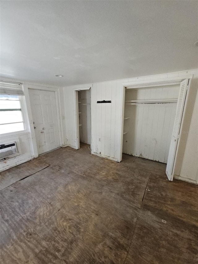 unfurnished bedroom with a wall mounted air conditioner and two closets