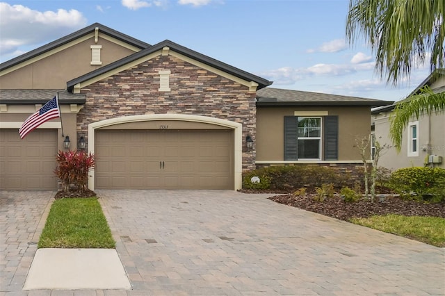 ranch-style house with a garage, stone siding, decorative driveway, and stucco siding