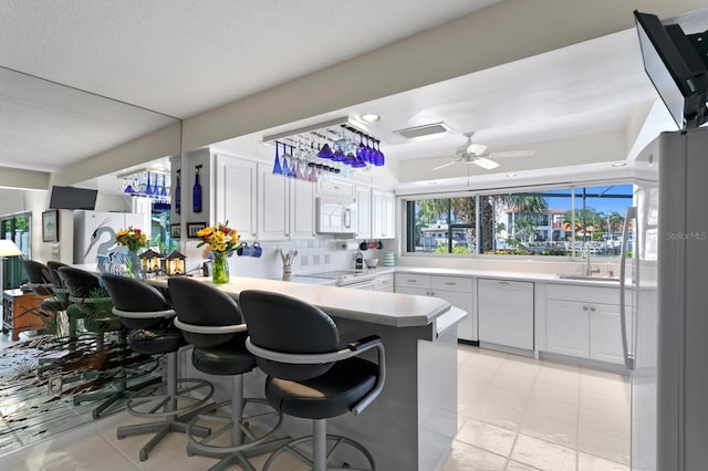 kitchen with white cabinetry, white appliances, kitchen peninsula, and a breakfast bar