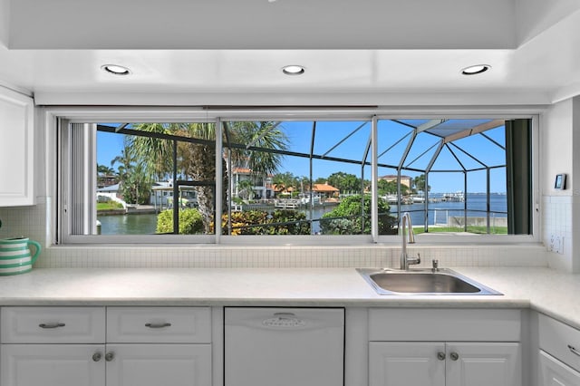 kitchen featuring sink, a water view, white dishwasher, decorative backsplash, and white cabinets