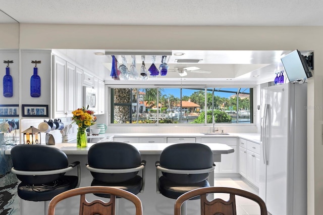 kitchen with a kitchen bar, sink, white appliances, ceiling fan, and white cabinets