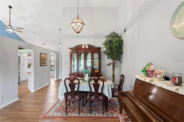 dining area with ceiling fan with notable chandelier, hardwood / wood-style floors, and high vaulted ceiling