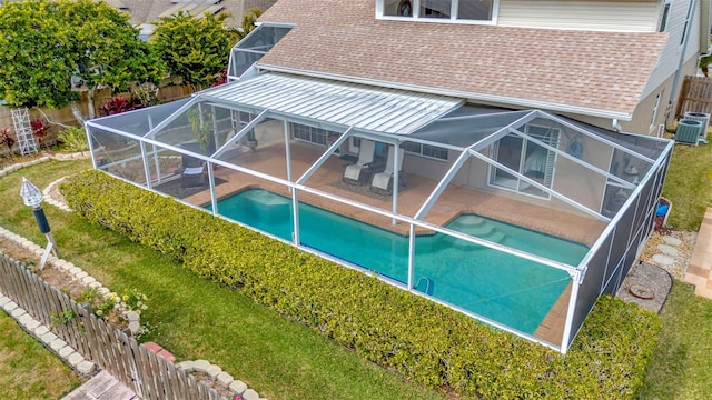 rear view of house with a lawn, cooling unit, glass enclosure, a fenced in pool, and a patio area