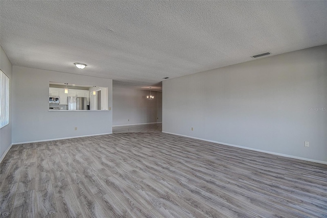 spare room with a chandelier, light hardwood / wood-style floors, and a textured ceiling