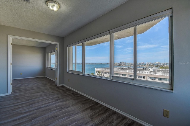 unfurnished room featuring a water view, dark hardwood / wood-style floors, and a textured ceiling