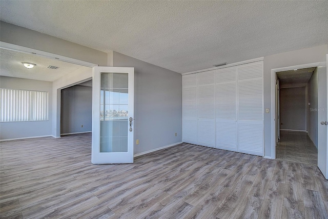 unfurnished bedroom featuring multiple windows, a closet, a textured ceiling, and light wood-type flooring