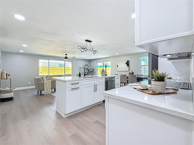 kitchen featuring pendant lighting, dishwasher, white cabinetry, sink, and light stone countertops