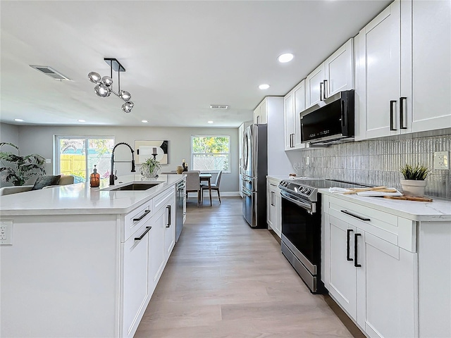 kitchen with appliances with stainless steel finishes, sink, white cabinets, hanging light fixtures, and a kitchen island with sink