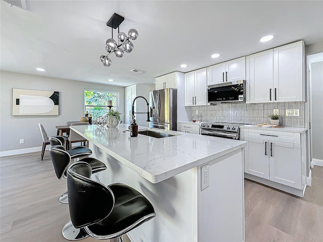 kitchen featuring decorative light fixtures, white cabinetry, a kitchen bar, stainless steel appliances, and a center island with sink