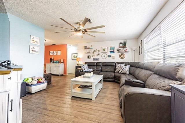 living room featuring ceiling fan, a textured ceiling, and light wood-type flooring