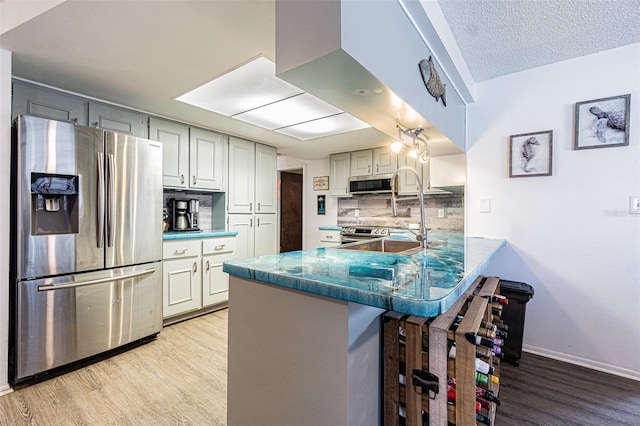 kitchen with a breakfast bar area, tasteful backsplash, appliances with stainless steel finishes, kitchen peninsula, and light hardwood / wood-style floors