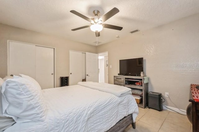 tiled bedroom featuring ceiling fan, a textured ceiling, and two closets