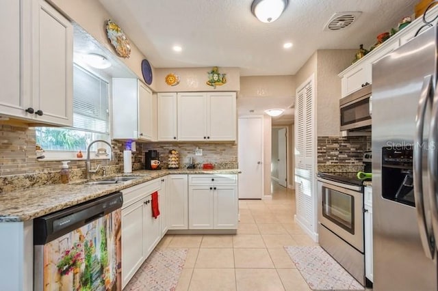 kitchen with sink, light stone counters, light tile patterned floors, appliances with stainless steel finishes, and white cabinets