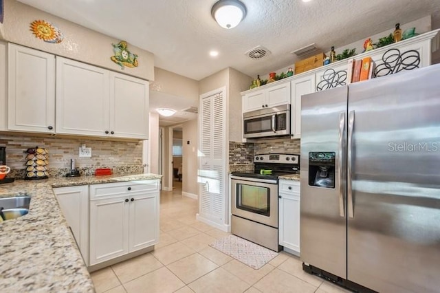 kitchen with light stone countertops, white cabinetry, appliances with stainless steel finishes, and light tile patterned flooring