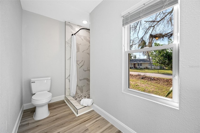 bathroom featuring a wealth of natural light, toilet, a marble finish shower, and wood finished floors