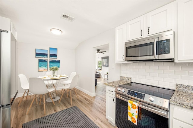 kitchen featuring appliances with stainless steel finishes, white cabinets, decorative backsplash, light stone countertops, and light wood-type flooring